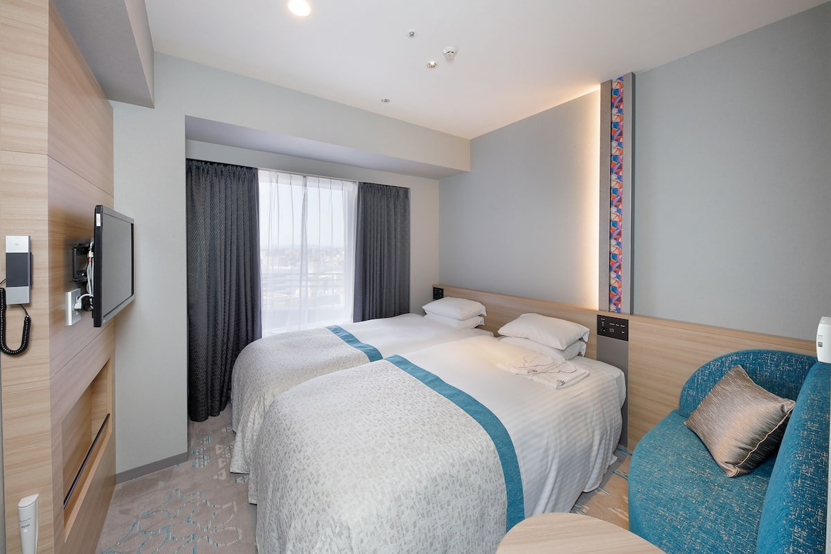 A hotel room with two beds, a TV, a desk with a phone, and a view of the city through the window.