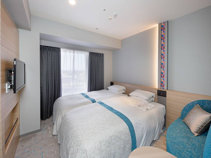 A hotel room with two beds, a TV, a desk with a phone, and a view of the city through the window.