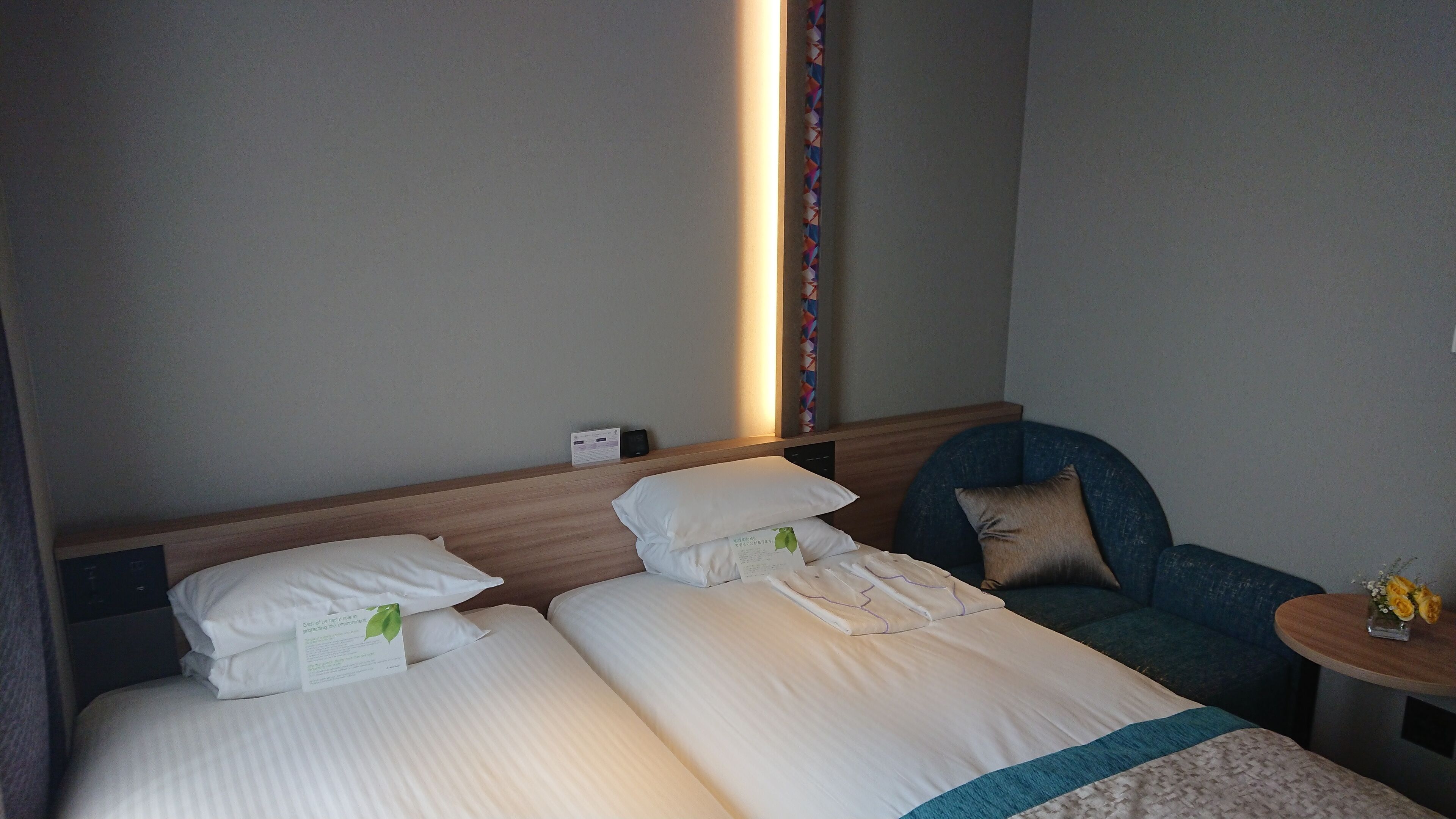 Una habitación de hotel con dos camas, una mesita de noche con un jarrón de flores y una silla.