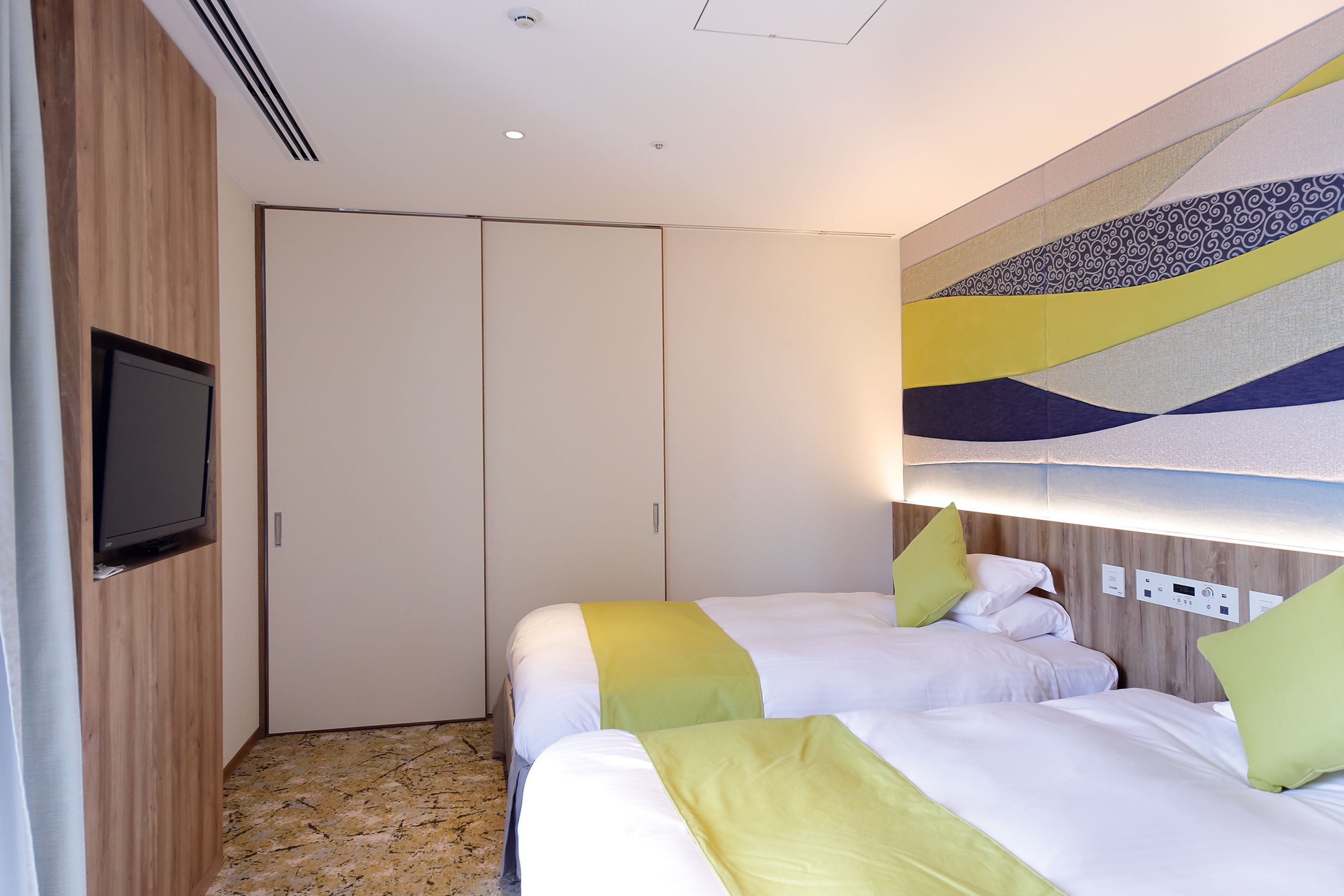 Habitación de hotel con dos camas, un televisor y un panel de control en la pared.