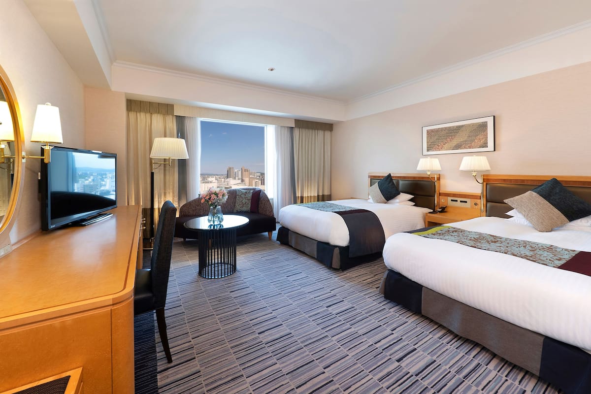 A hotel room with two beds, a desk, a TV, and a view of the city.