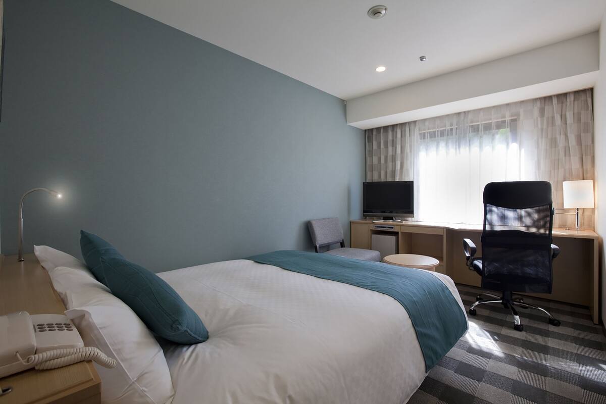 Une chambre d’hôtel avec un lit, un bureau, une télévision et une chaise.
