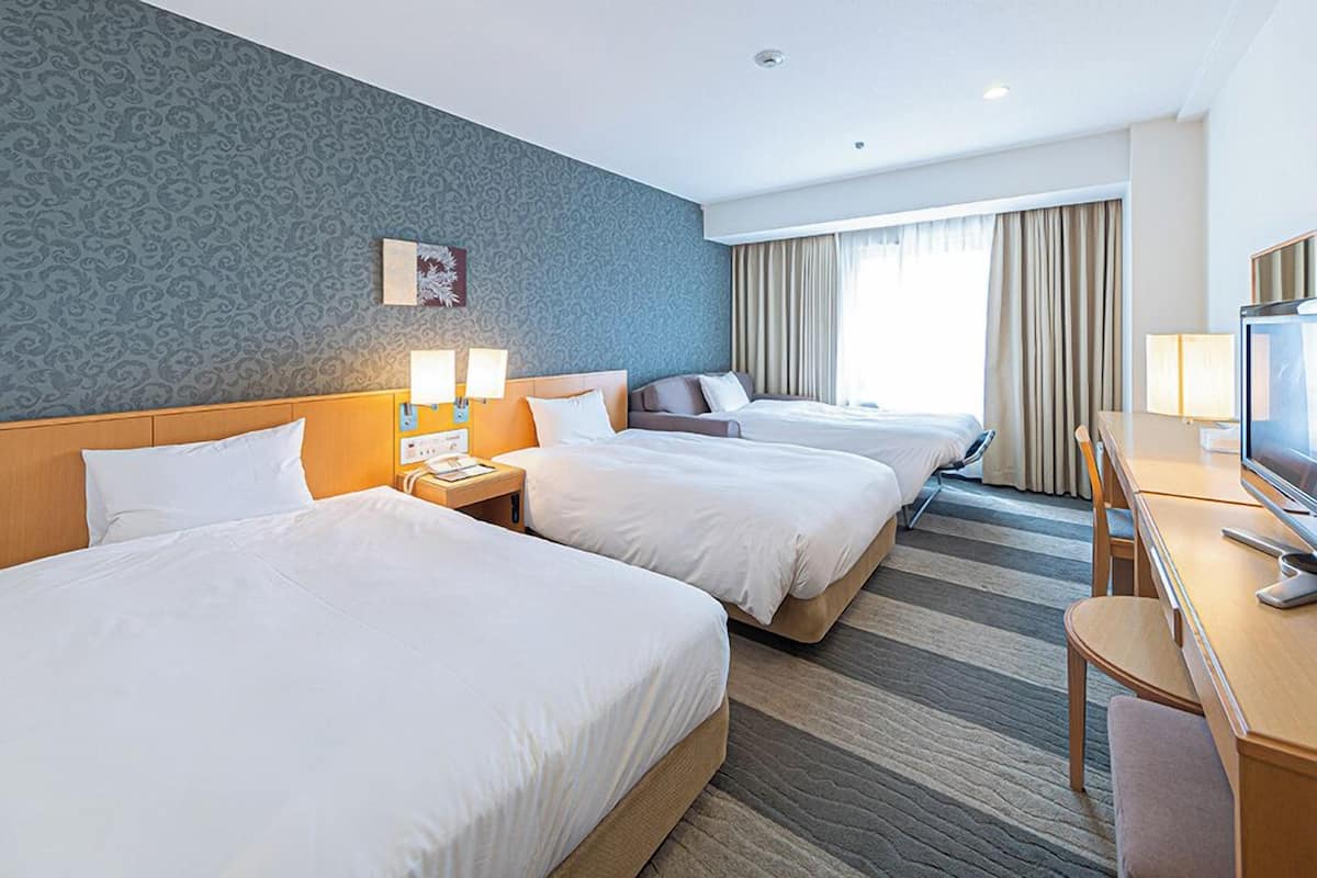 Une chambre d’hôtel avec deux lits, un bureau, une télévision et une fenêtre avec des rideaux.