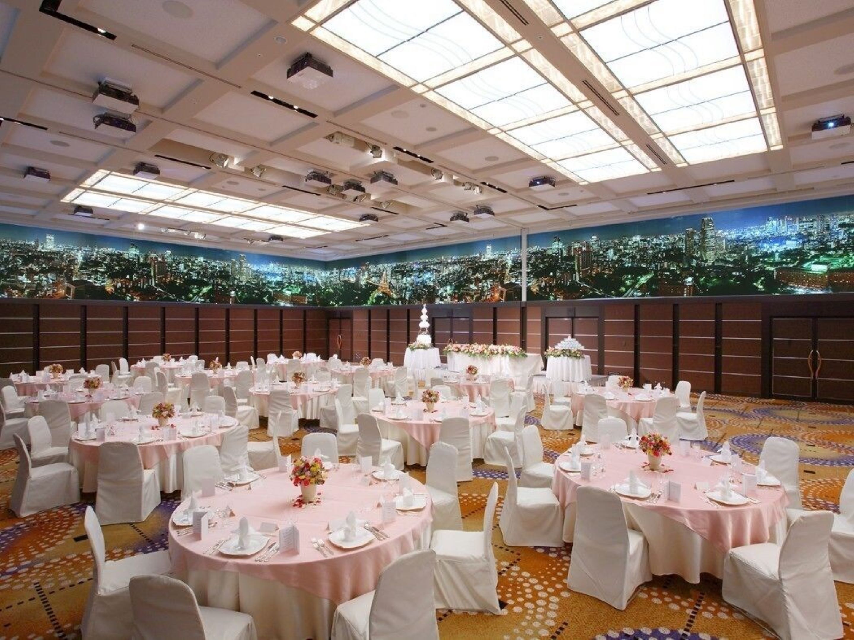 A banquet hall with round tables, white chairs, and a cityscape view.