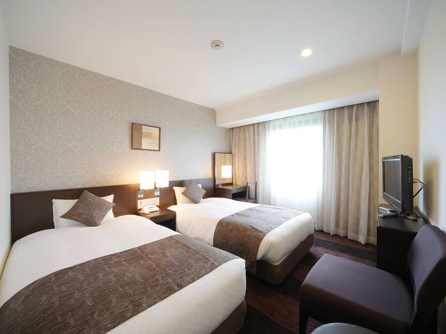A hotel room with two beds, a TV, a desk, and a chair.