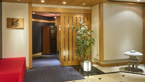 Un espace d’accueil doté d’une porte en bois, d’un comptoir de réception, d’une plante en pot et d’une lanterne décorative en pierre.