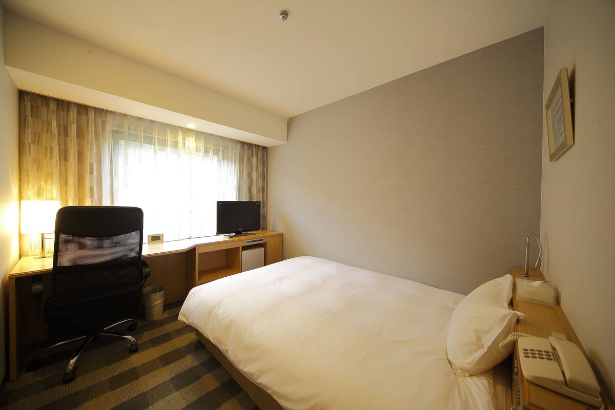 Une chambre d’hôtel comprenant un lit, un bureau avec un ordinateur, une chaise et un téléphone.