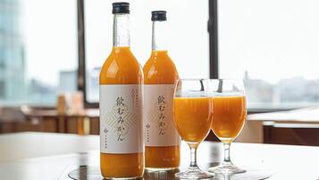 Two bottles of orange juice and two glasses on a table with a view of a cityscape.