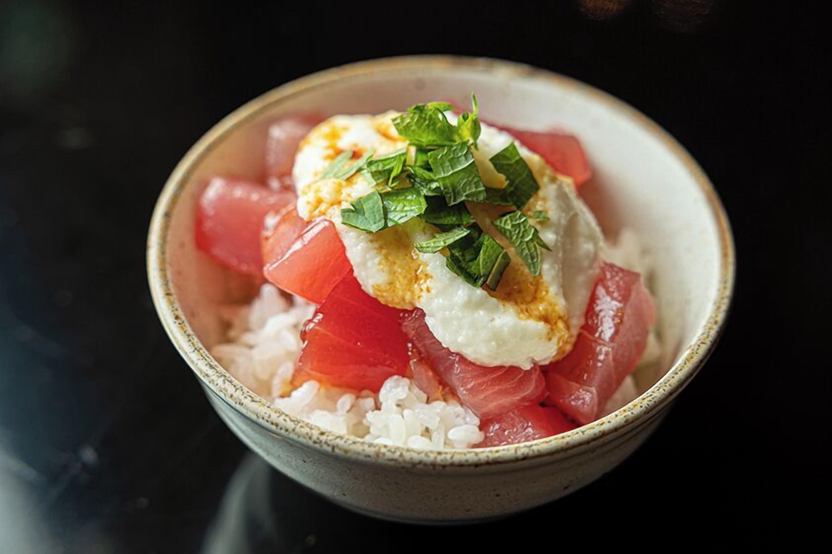 A bowl of rice topped with a poached egg, diced tomatoes, and green herbs.