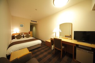 Habitación de hotel con cama, escritorio, silla, televisor y un refrigerador pequeño.