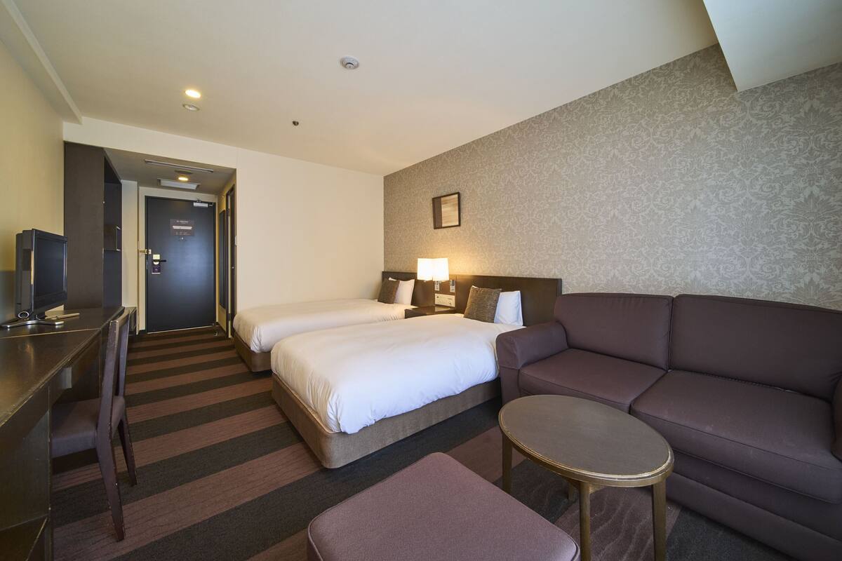 Une chambre d’hôtel avec deux lits, un canapé, une petite table, une télévision et un bureau.