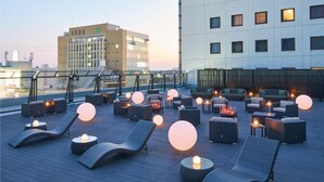 Un espace de détente sur le toit, aménagé avec des fauteuils, des tables rondes et un éclairage d’ambiance.