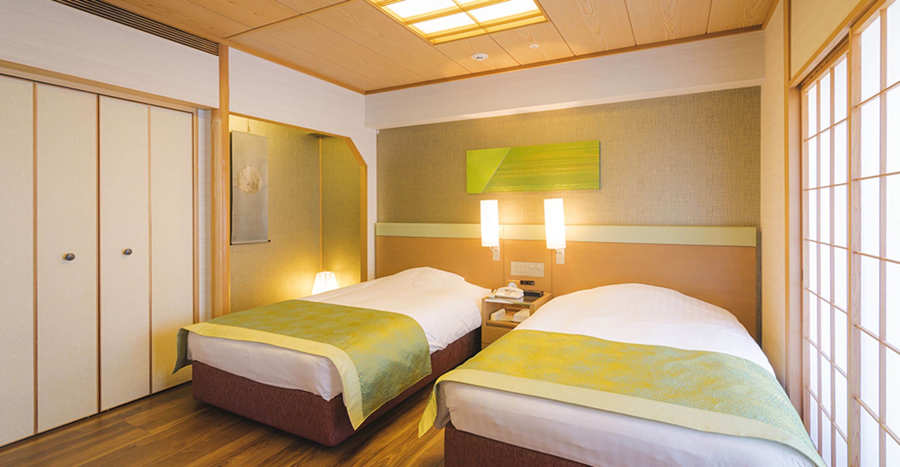A hotel room with two beds, wooden flooring, a large window, and a wall-mounted artwork.