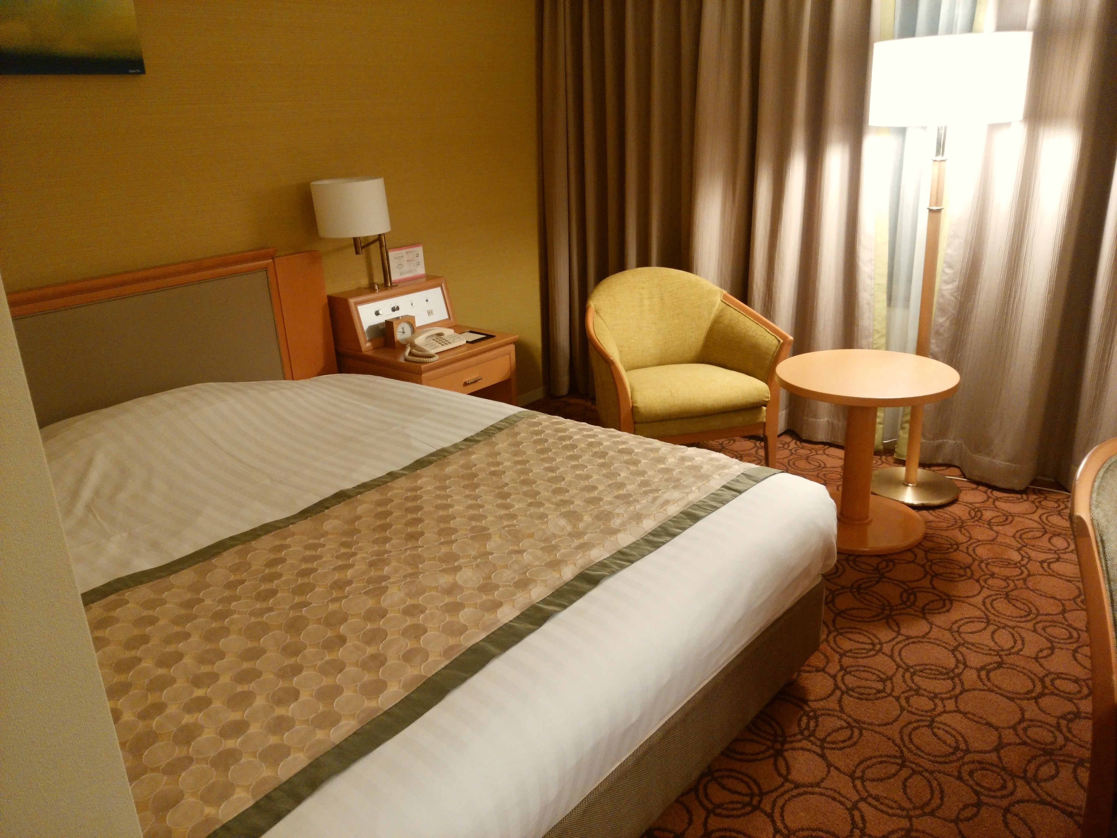 A hotel room with a bed, a chair, a bedside table with a lamp, and a small round table.