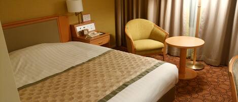 A hotel room with a bed, a chair, a bedside table with a lamp, and a small round table.