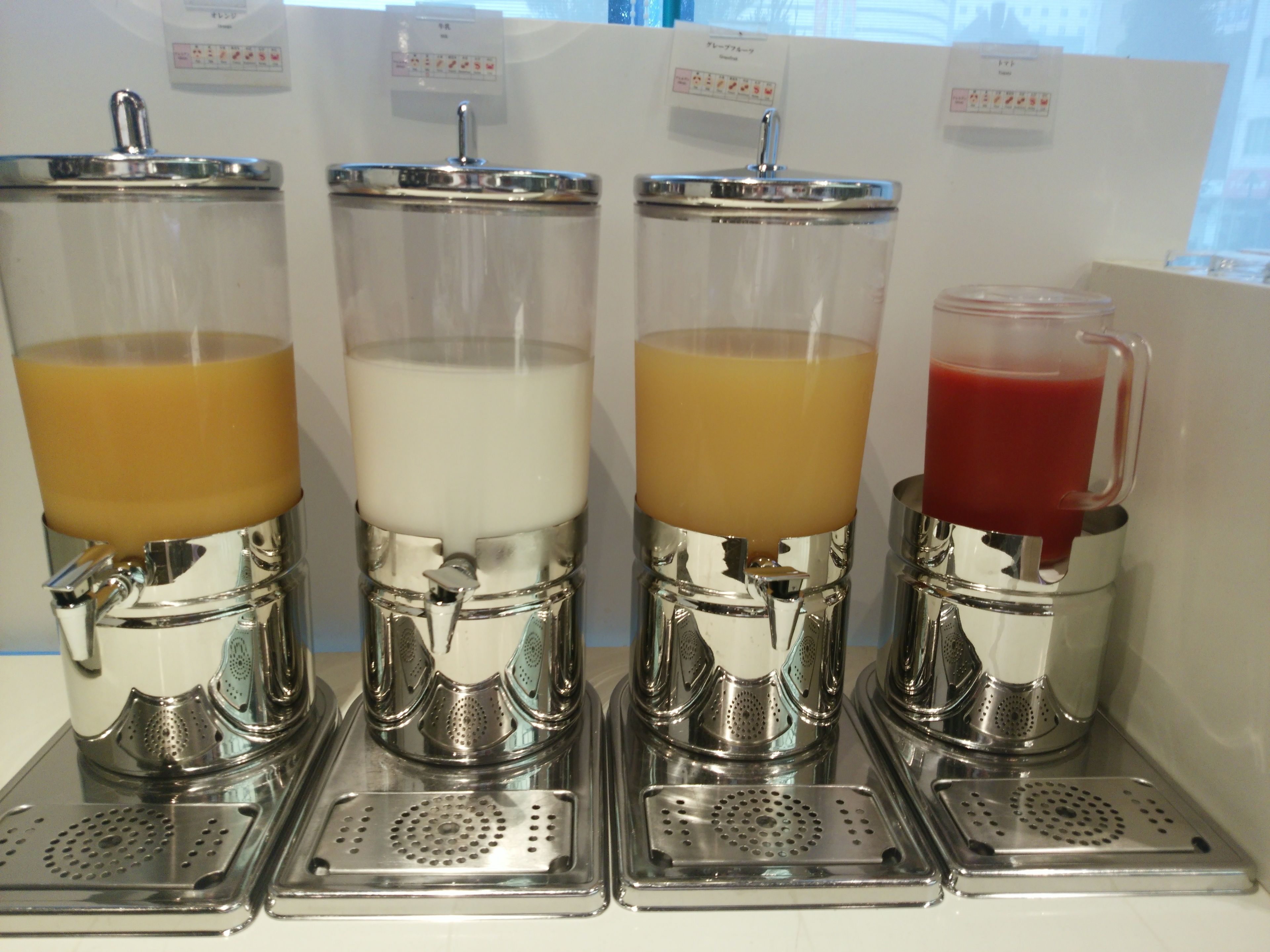 Four beverage dispensers with spouts and metal grates.