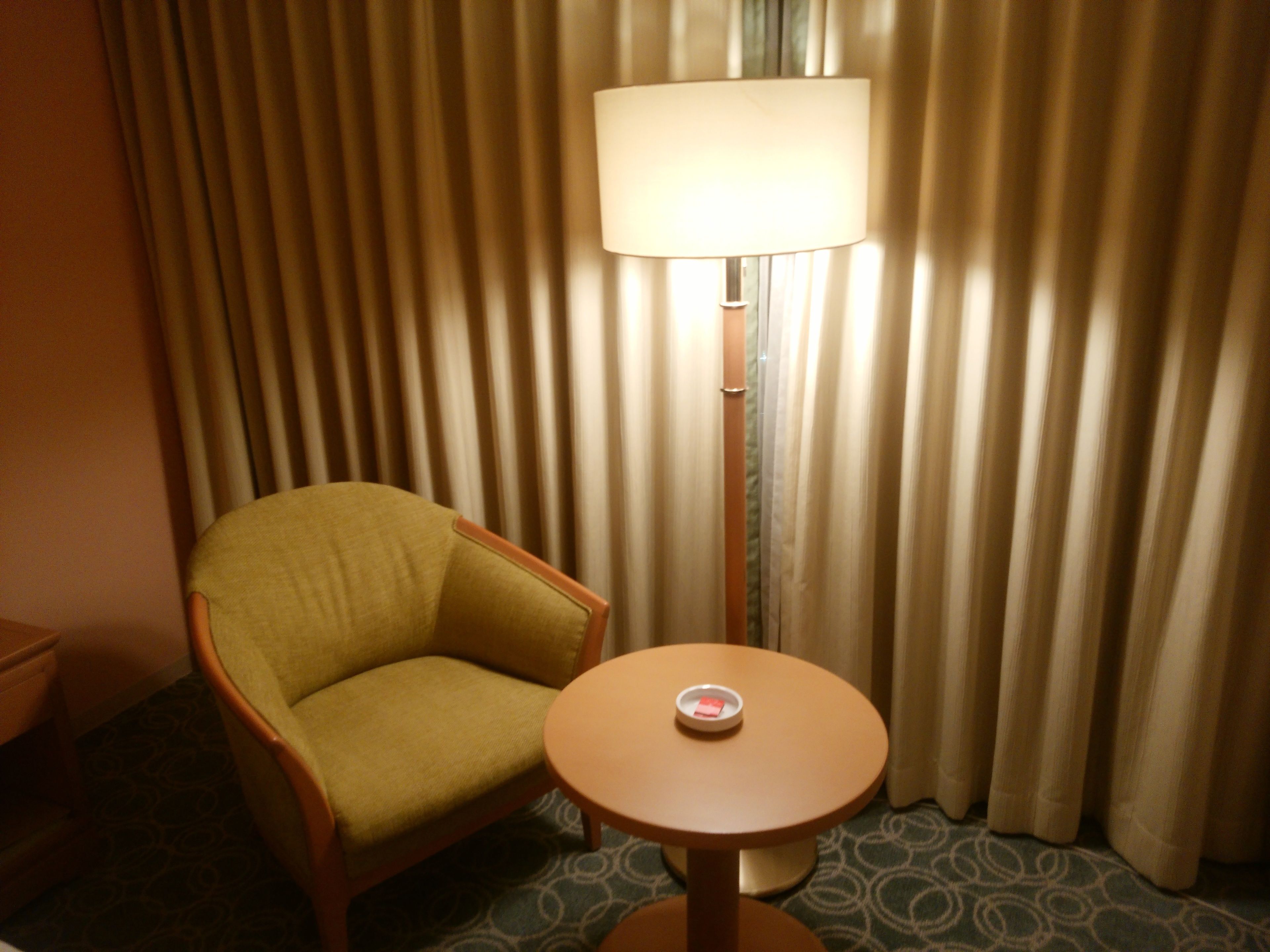 A room with a green armchair, a small round table with a lamp, and a curtain backdrop.