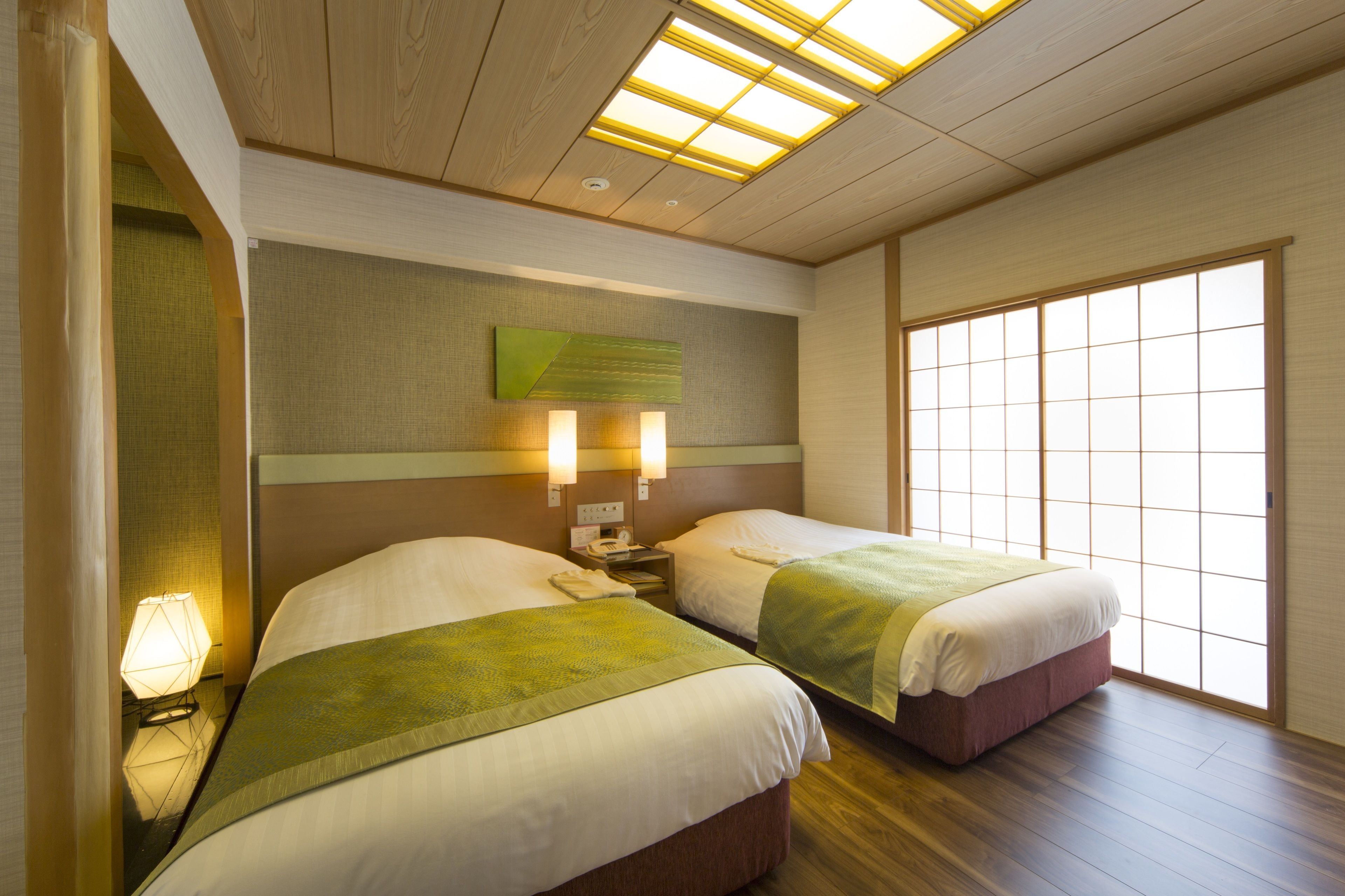 A hotel room with two beds, a nightstand, a lamp, a wall-mounted phone, and a large window.