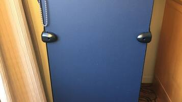 Uma mala azul com rodinhas e alça, encostada em uma parede com carpete estampado.