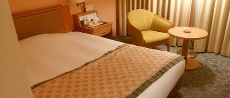 A hotel room with a bed, a chair, a bedside table with a lamp, a phone, and a small table with a cup.