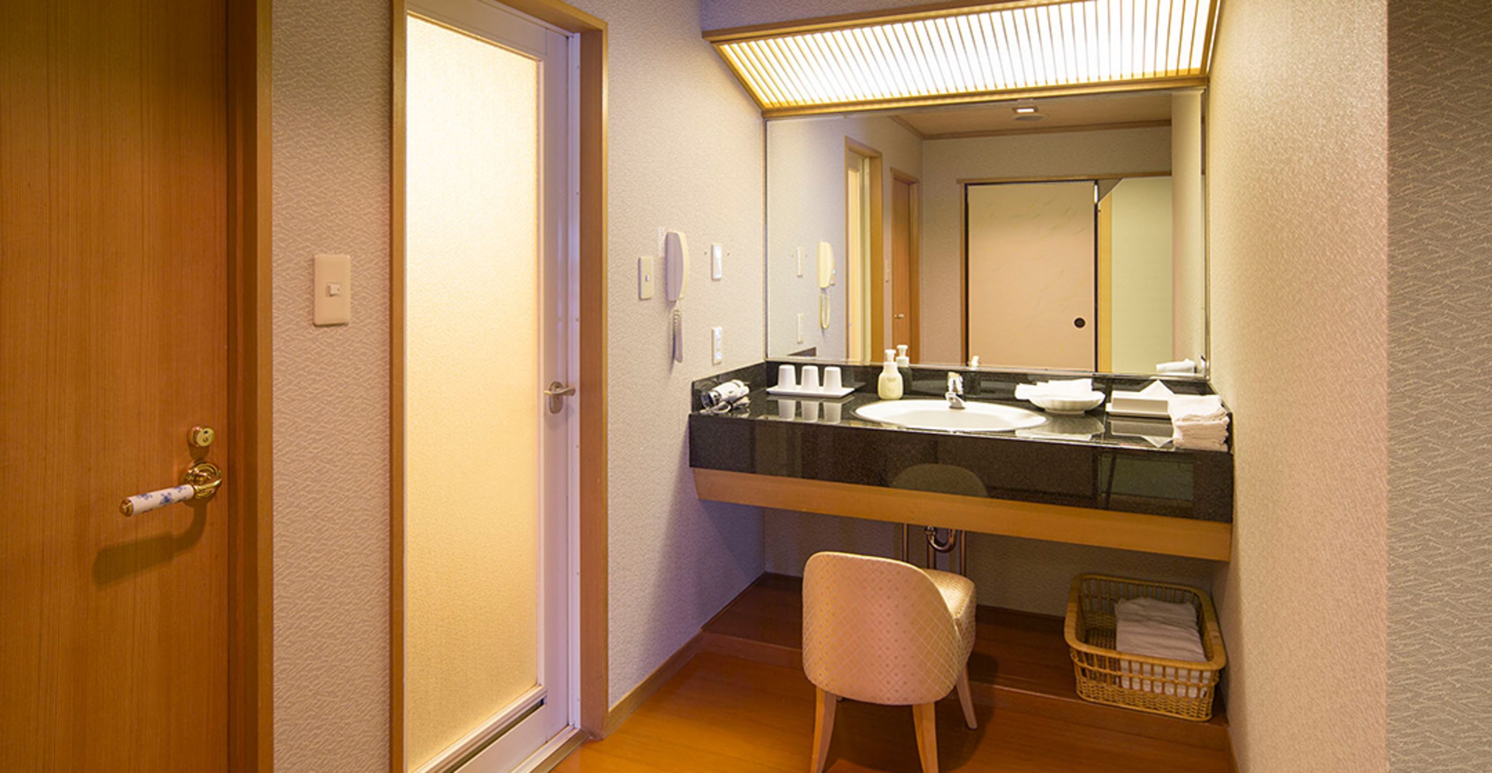 A bathroom with a wooden door, a sink, a mirror, and a wicker basket.