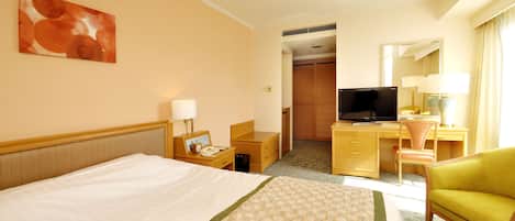 A hotel room with a bed, a desk with a computer, a television, and a chair.