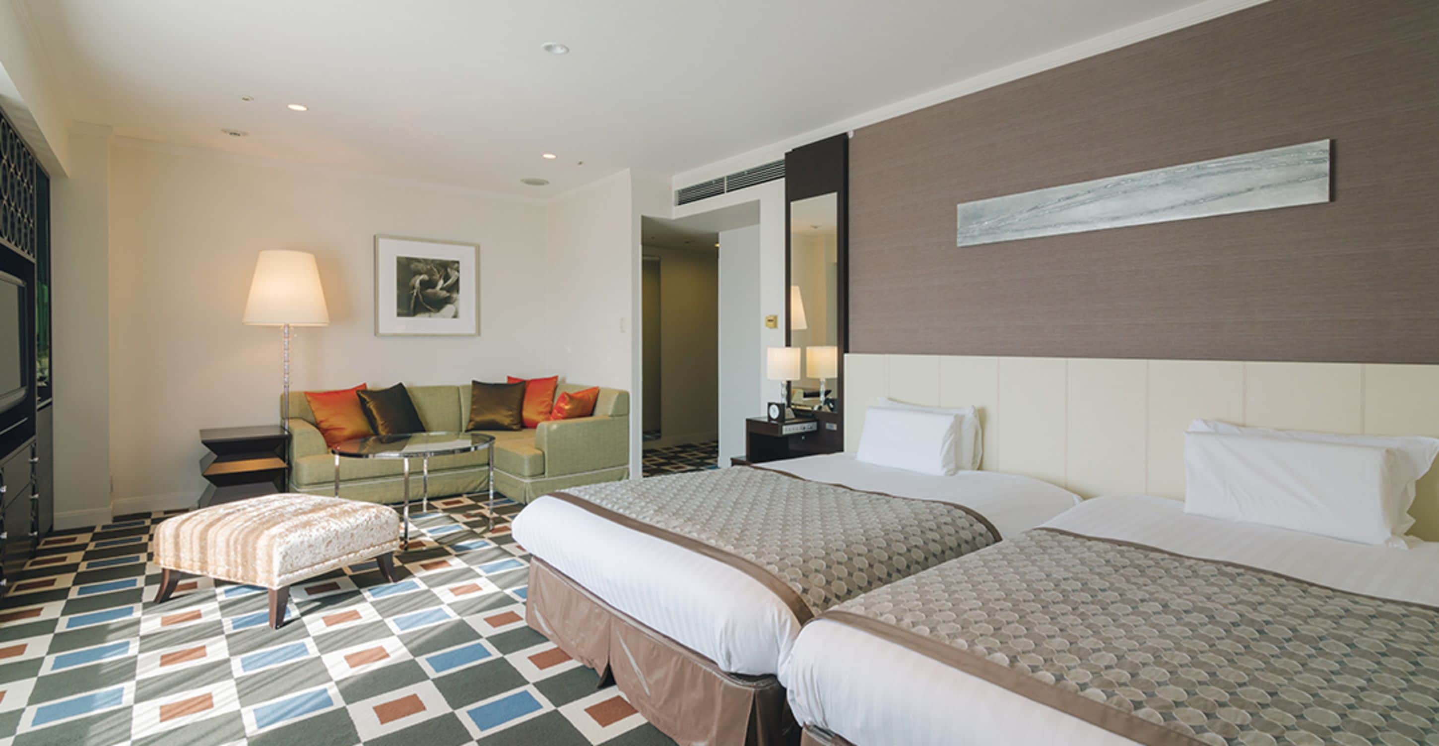 Hotelkamer met twee bedden, een bank, een kleintje tafeltje en een vloer met patroon.