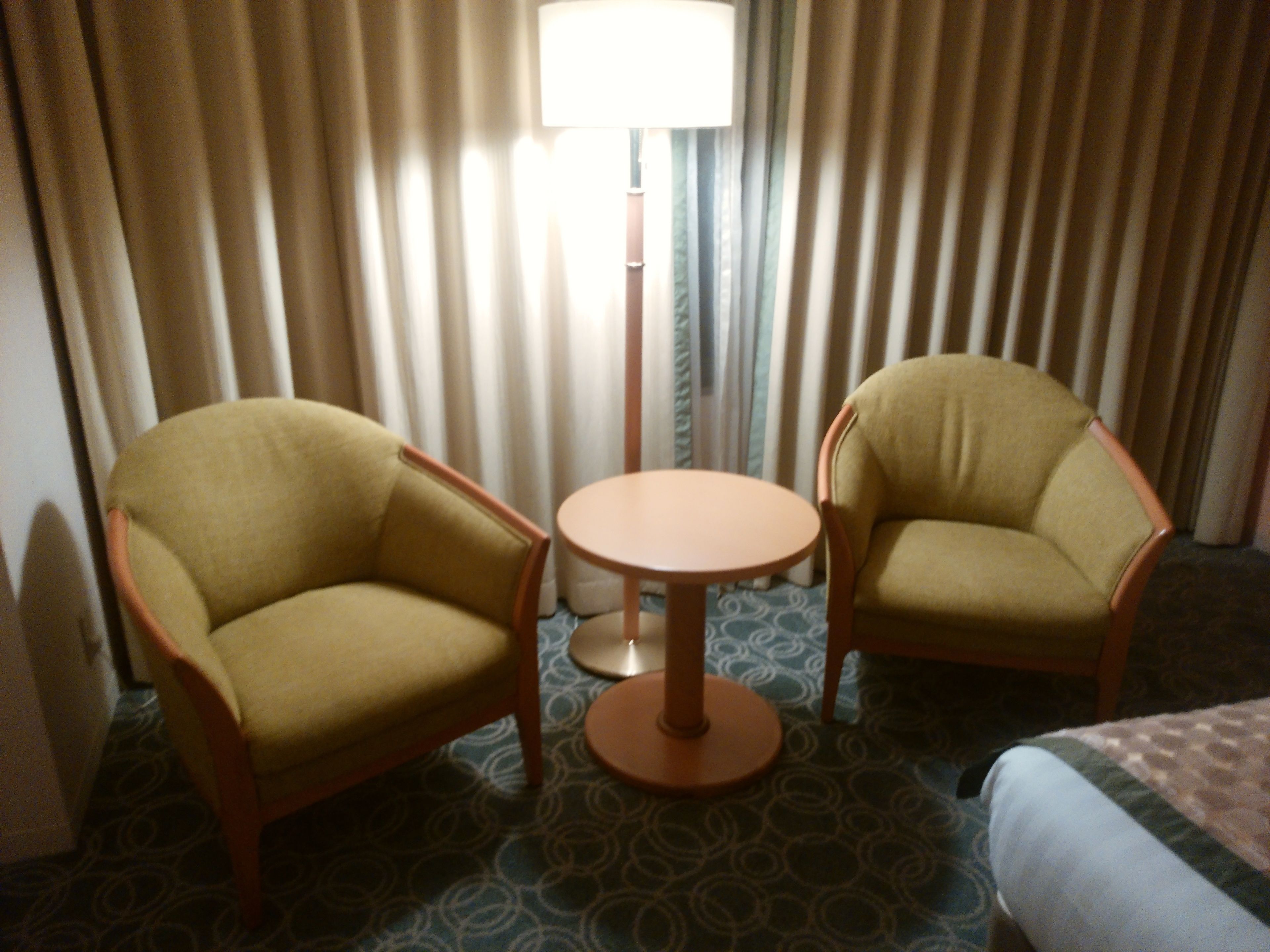 Una habitación de hotel con dos sillones, una mesa redonda pequeña y una cama.