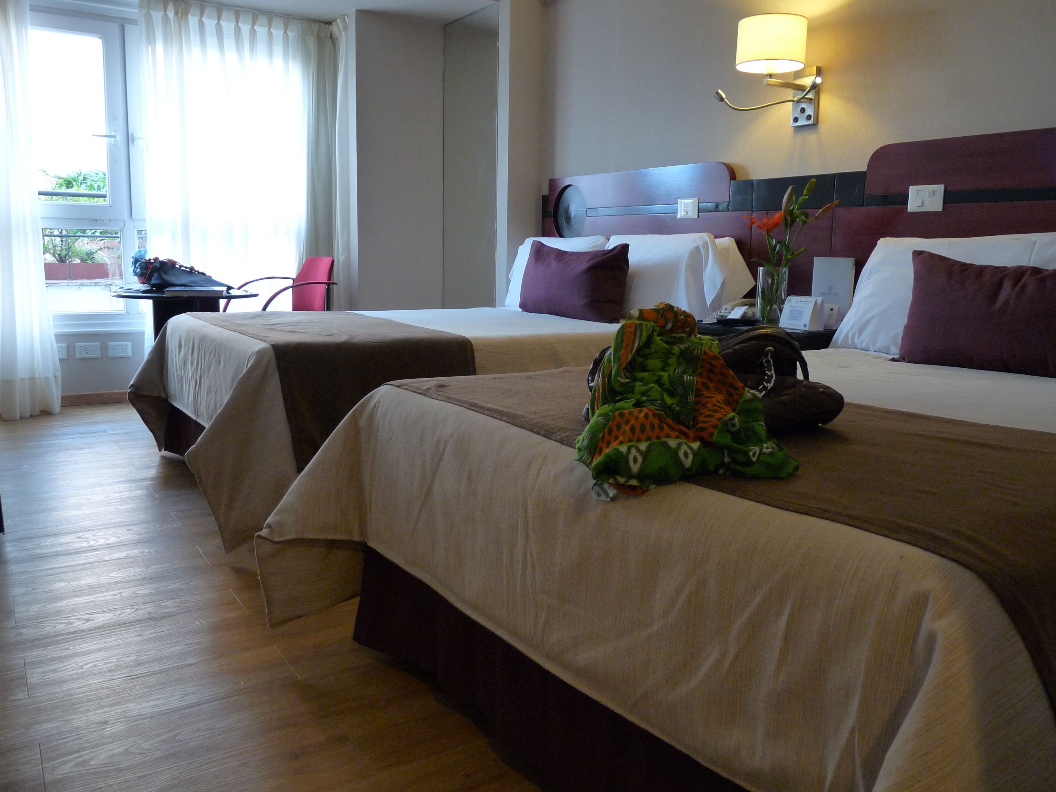 A hotel room with two beds, a desk, a chair, and a window with curtains.