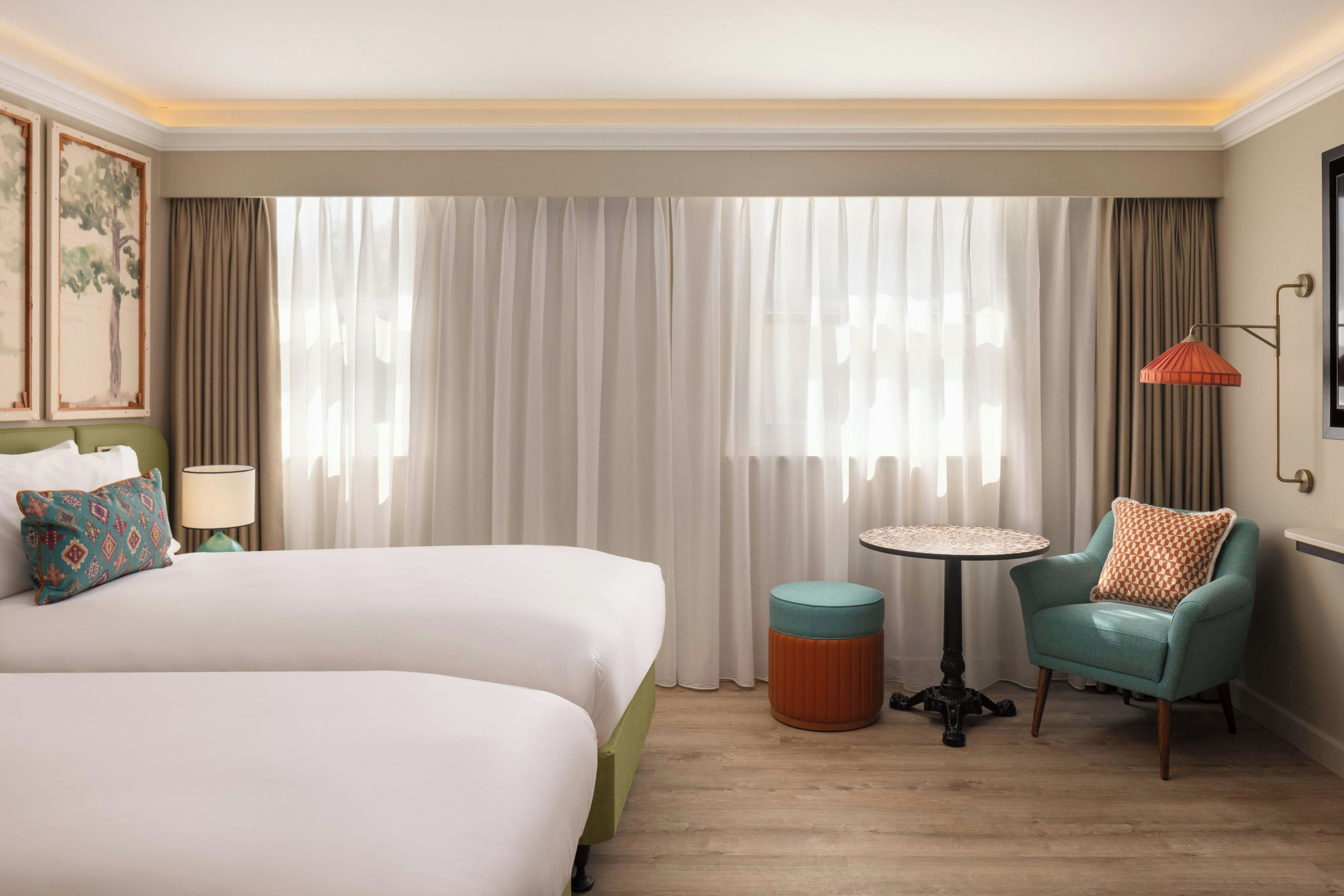 Una habitación de hotel con dos camas, una mesa redonda, una silla y una lámpara.