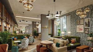 A spacious lounge area with multiple seating options, including sofas and armchairs, arranged around a central coffee table. There are several pendant lights hanging from the ceiling, and the walls are adorned with framed artwork. - Hyde & Seek, London Hyde Park, a Tribute Portfolio Hotel (London)