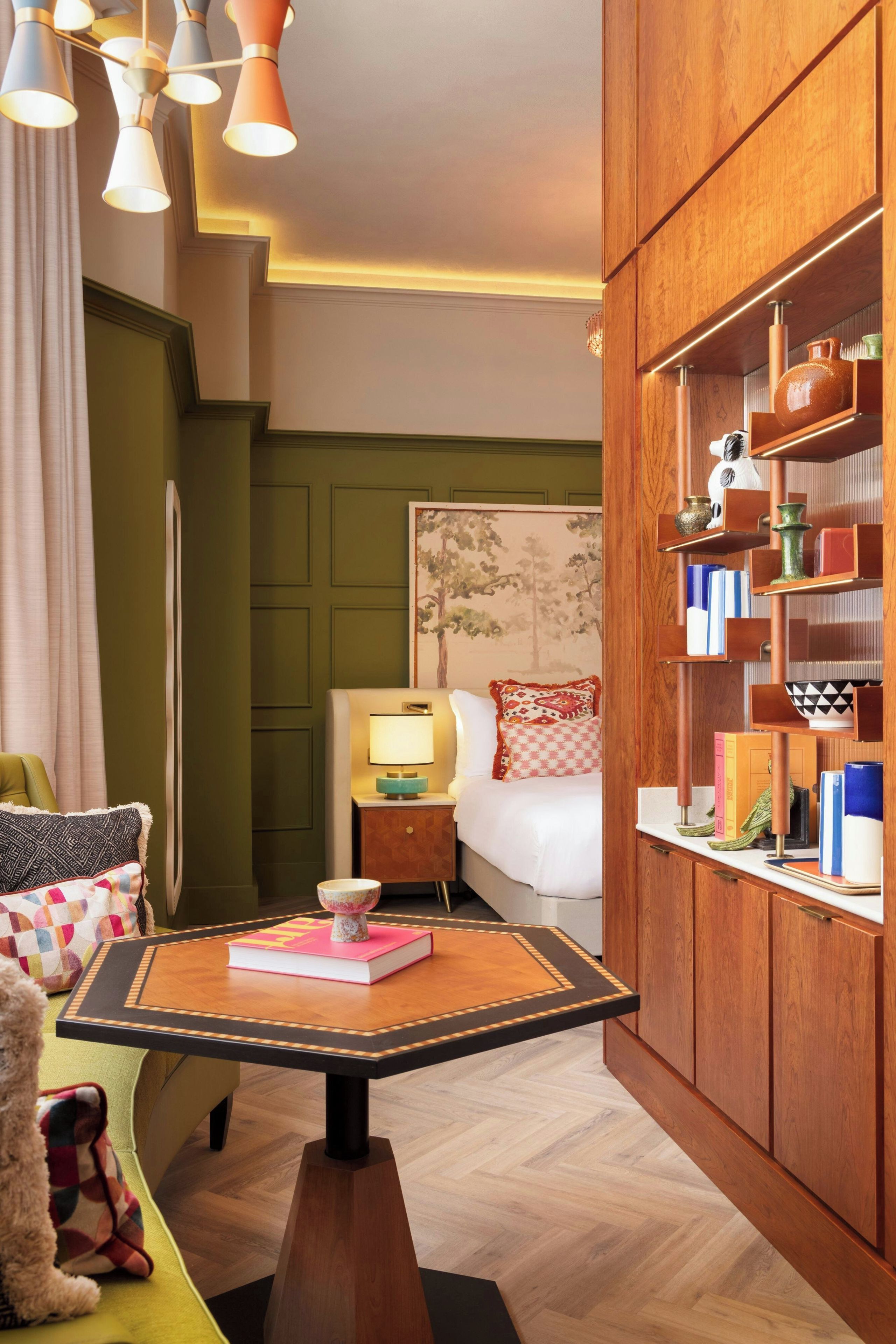 A hotel room with a wooden cabinet, a bed with a headboard, a nightstand, a table with a book, and a teddy bear.