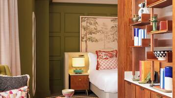 A hotel room with a wooden cabinet, a bed with a headboard, a nightstand, a table with a book, and a teddy bear.