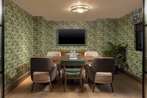A dining area with a round table, four chairs, a flat-screen TV mounted on the wall, and a potted plant. - Hyde & Seek, London Hyde Park, a Tribute Portfolio Hotel (London)