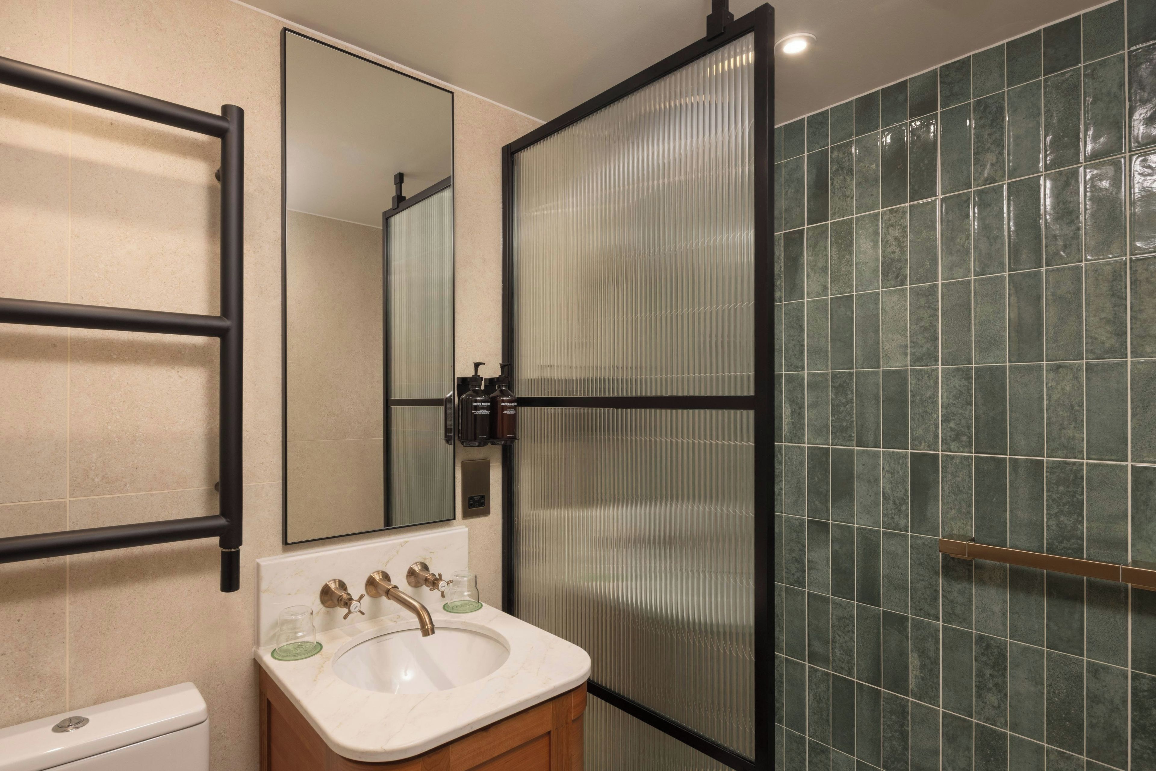 A bathroom with a white sink, a mirror, a toilet, and a shower area with green tiles.