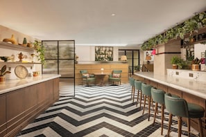 Een moderne keuken met een zwart-wit visgraatvloer, houten keukenkastjes en groene barkrukken.