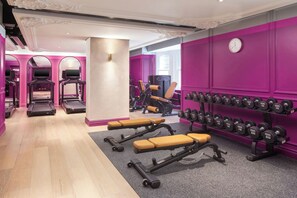 Een sportschool met loopbanden, gewichtbanken en een muur vol dumbbells.