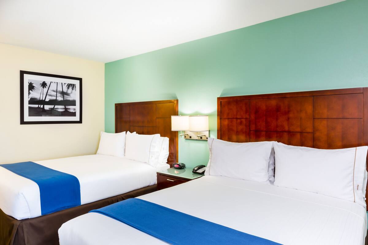 Habitación de hotel con dos camas, una mesita de noche con lámpara, un teléfono y un cuadro en la pared.