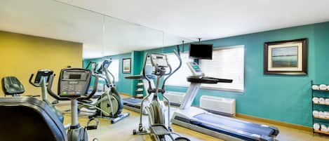 Un gimnasio con diversos equipos de ejercicio, como cintas de correr, bicicletas estáticas y elípticas.