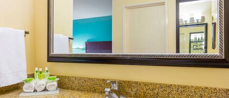 A bathroom with a granite countertop, a white sink, a mirror, and a towel rack with towels and toiletries.
