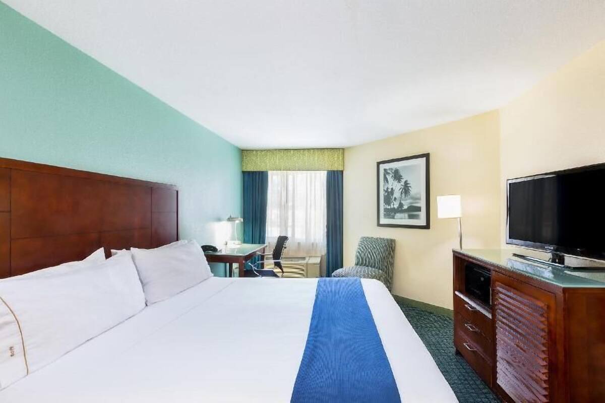Habitación de hotel con una cama grande, un escritorio, una silla, un televisor y un cuadro en la pared.