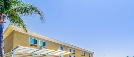 A multi-story hotel with a yellow facade, covered outdoor seating area, and a parking lot.