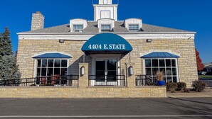 Un edificio con fachada de piedra, toldo azul con la señalización "4404 E. STATE" y un cielo azul despejado.
