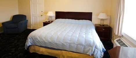 A hotel room with a bed, two bedside tables with lamps, a chair, a door, and a window with curtains.