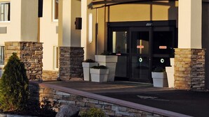 A hotel entrance with a covered walkway, stone pillars, and a glass door with a sign.
