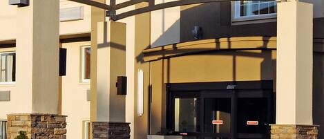 A hotel entrance with a covered walkway, stone pillars, and a glass door with a sign.