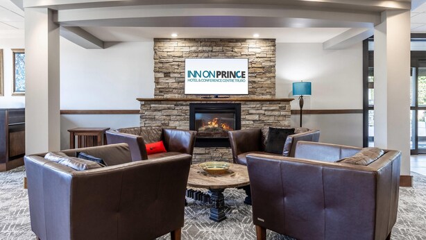 A modern lounge area with leather sofas, a central coffee table, a stone fireplace, and a sign for 'INN ON PRINCE HOTEL & CONFERENCE CENTRE TRURO.'
