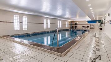 An indoor swimming pool with tiled walls, a blue pool, and a tiled floor.