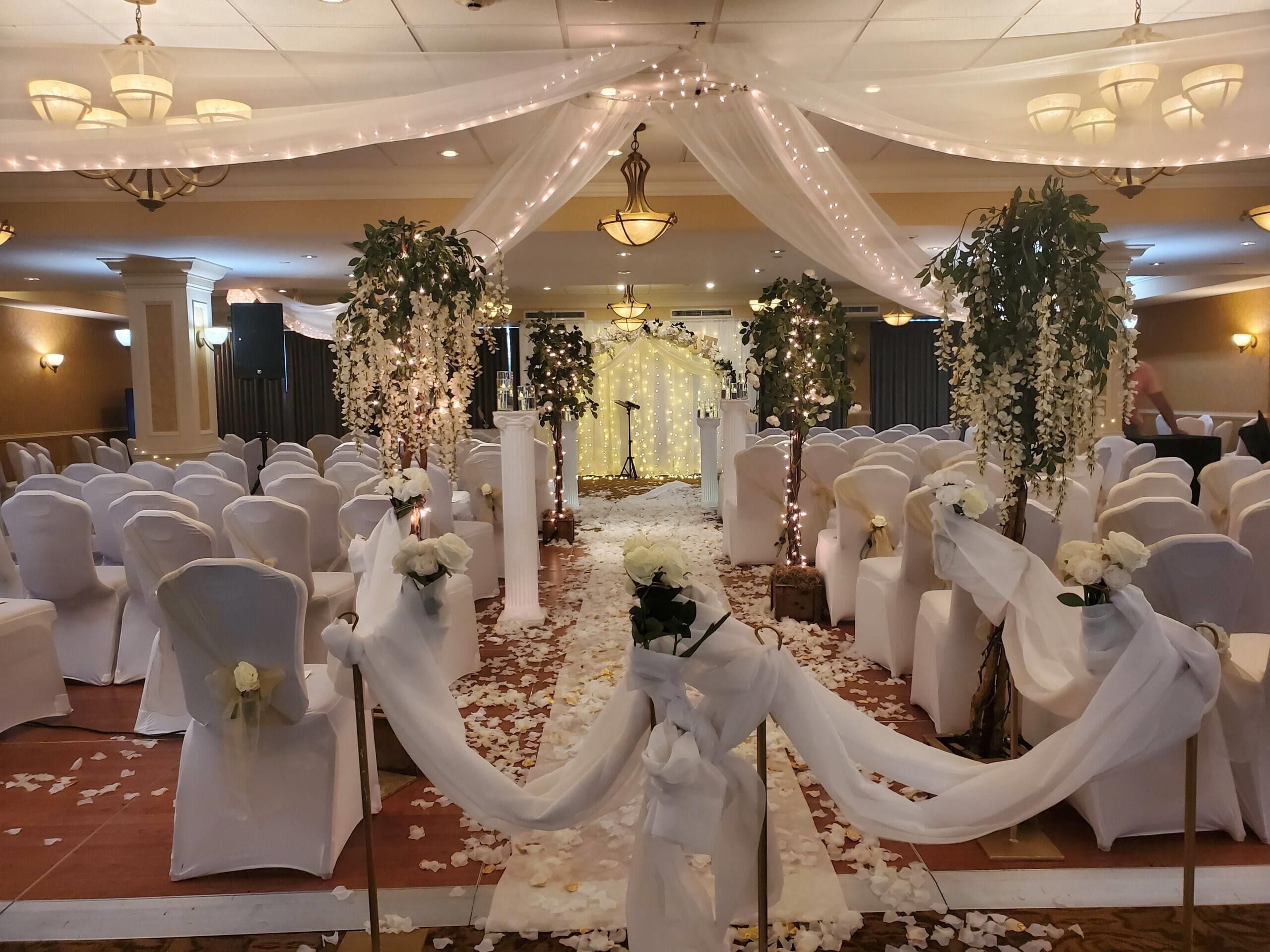 A wedding venue with white chairs, a flower-decorated aisle, and chandeliers.
