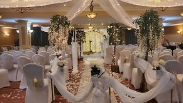 Un lieu de réception pour mariages avec des chaises blanches, une allée décorée de fleurs et des lustres.